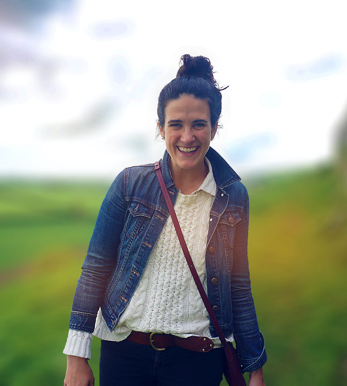 Photo of Micaela with greenery behind her, smiling at camera, wearing a denim jacket and white shirt with hair up.