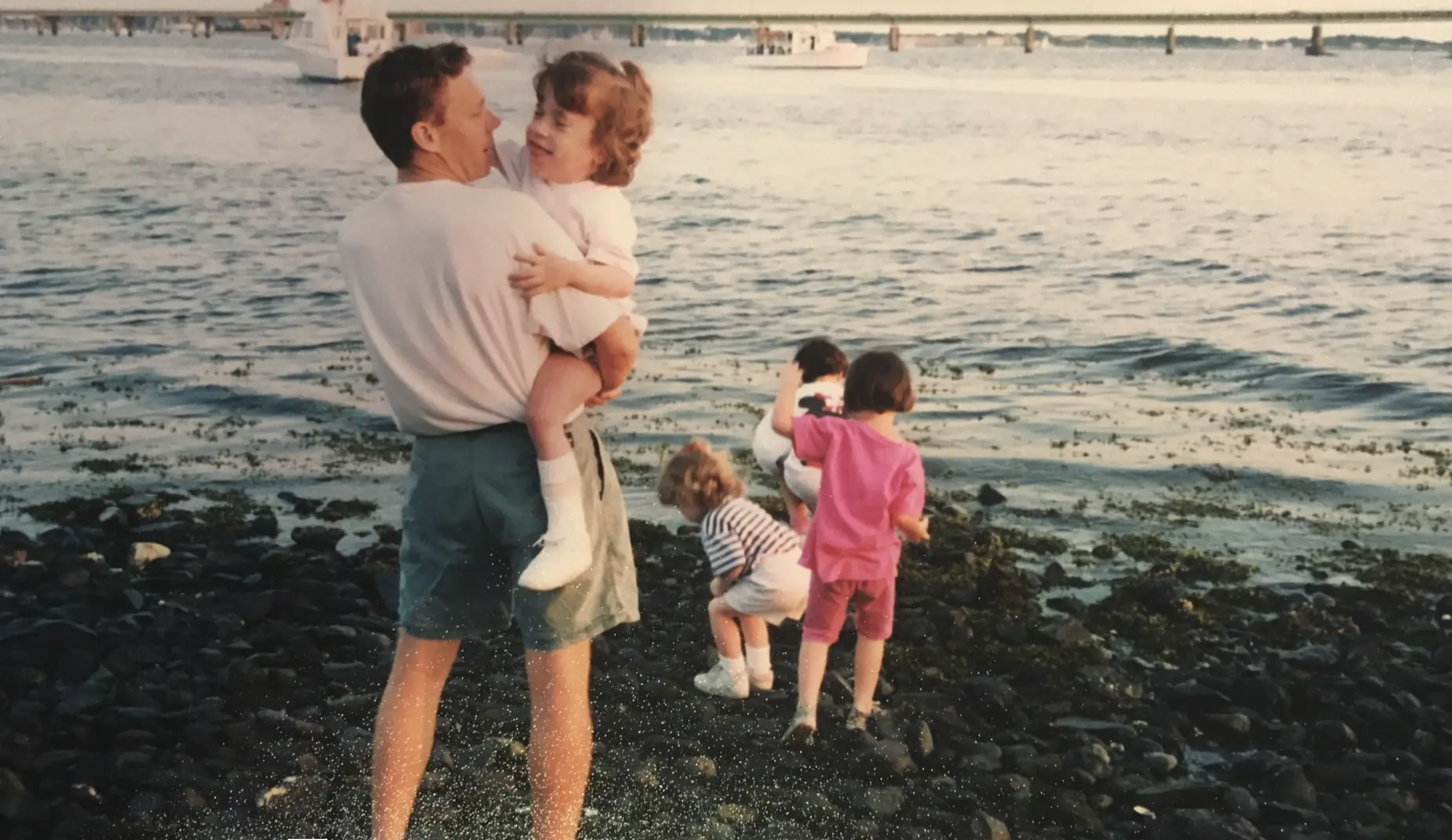 Picture of Kelsey as a child being carried by her dad with other children at the waters edge.