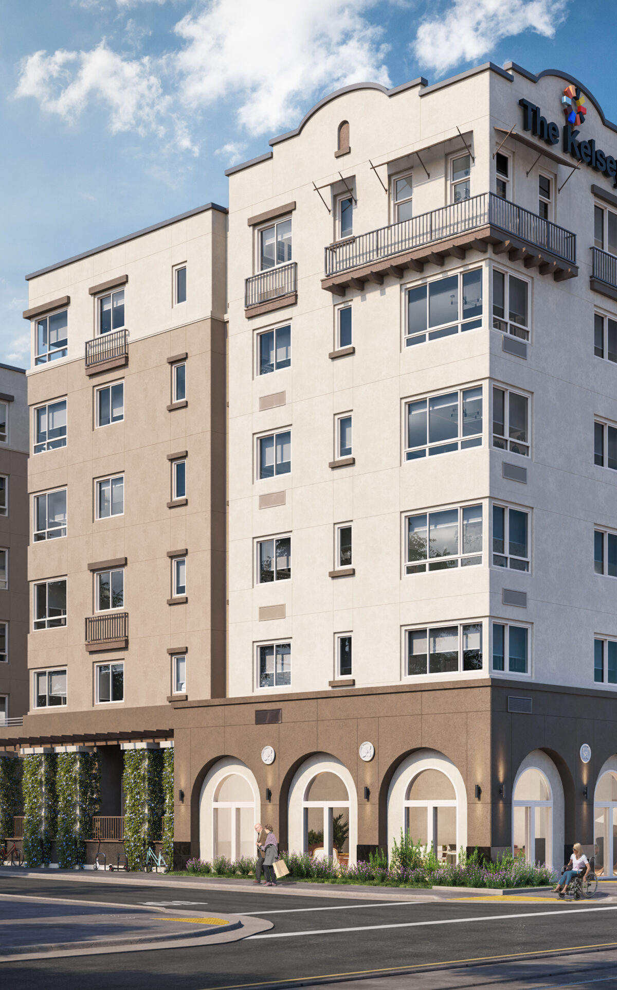 The exterior of The Kelsey Ayer Station, a tan and brown building with windows, small balconies, and arched windows and greenery on the bottom floor. A sign on the top says "The Kelsey" with our brandmark above it. A train is in the bottom right corner about to pass by and people using wheelchairs and walking are on the street.