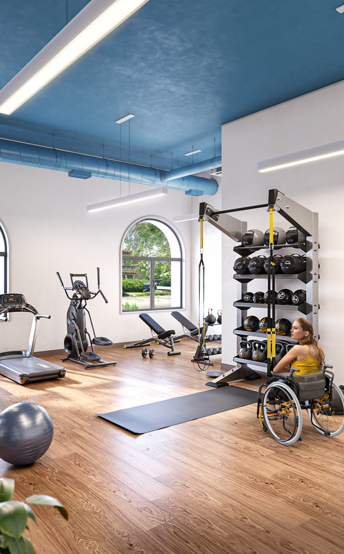 The fitness room at The Kelsey Ayer Station with equipment, weights, plants, and lights. There is a person running and a person using a wheelchair in the weight areas. Windows overlook the street and trees.