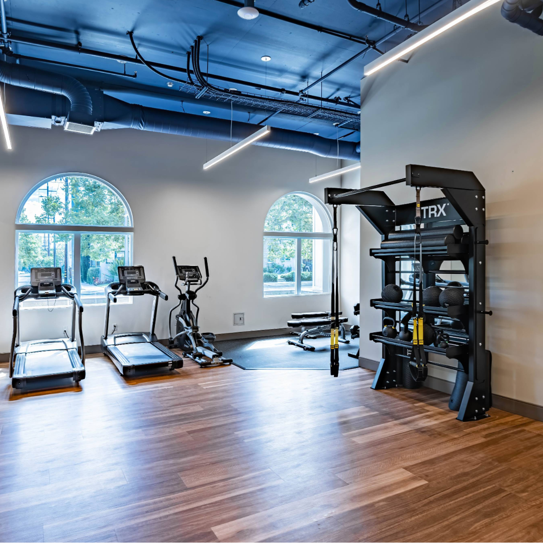 A picture of the exercise room in The Kelsey Ayer Station. Exercise equipment such as treadmills and weights are visible. Windows can be seen on one of the walls.