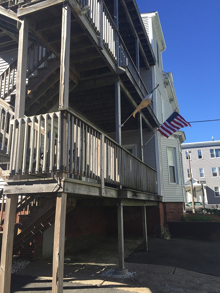 Image of a wooden staircase and deck on the back of a house. An American flag is pictured on side of home.