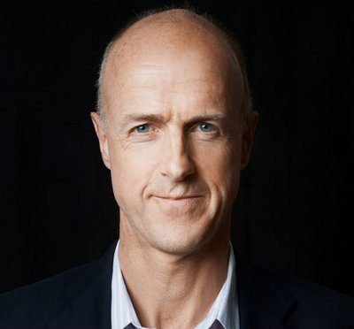 Johnn O'Farrell, a light-skinned man wearing a dark suitcoat and a light-colored dress shirt is pictured against a dark background