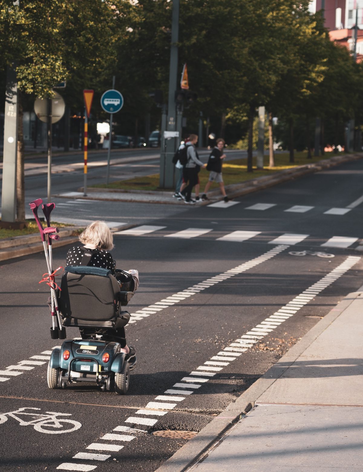 lady in power chair storing crutches in the back of her chair as she drives down the street using bike lane.