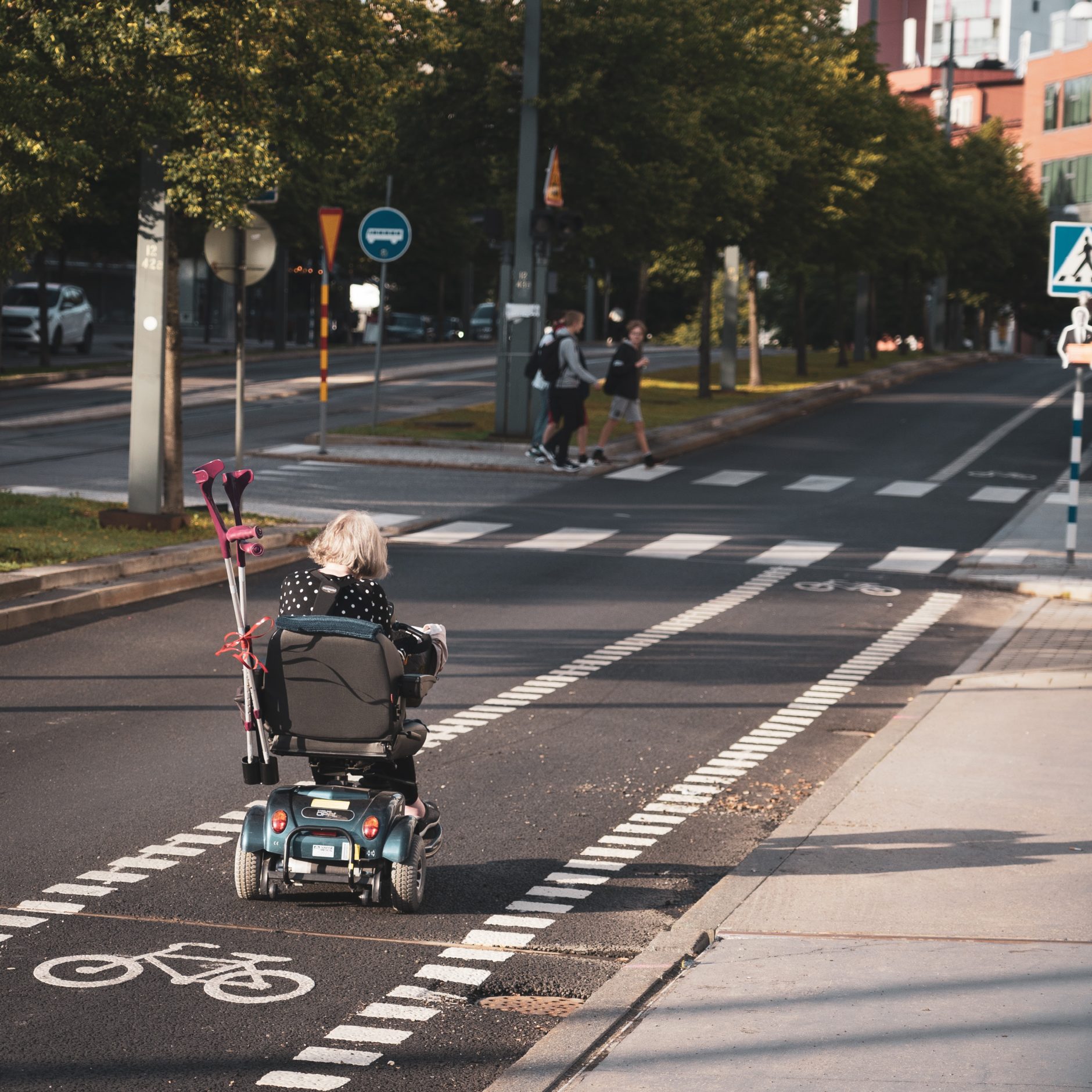 lady in power chair storing crutches in the back of her chair as she drives down the street using bike lane.