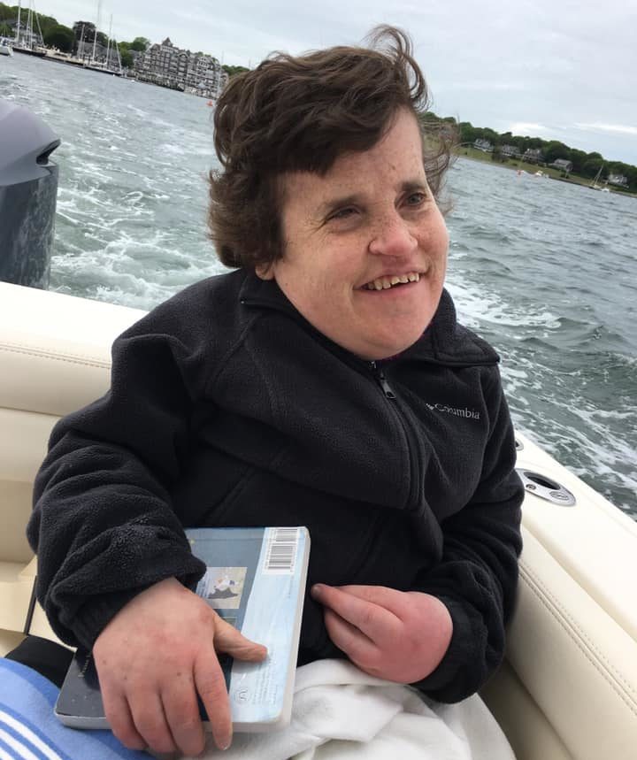 Kelsey sitting on a boat, waves behind her, she's smiling holding a book, she has a black jacket with short dark hair.