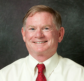 Steve, a light skinned man, is pictured against a gray background wearing a light colored shirt and red tie. He is smiling.