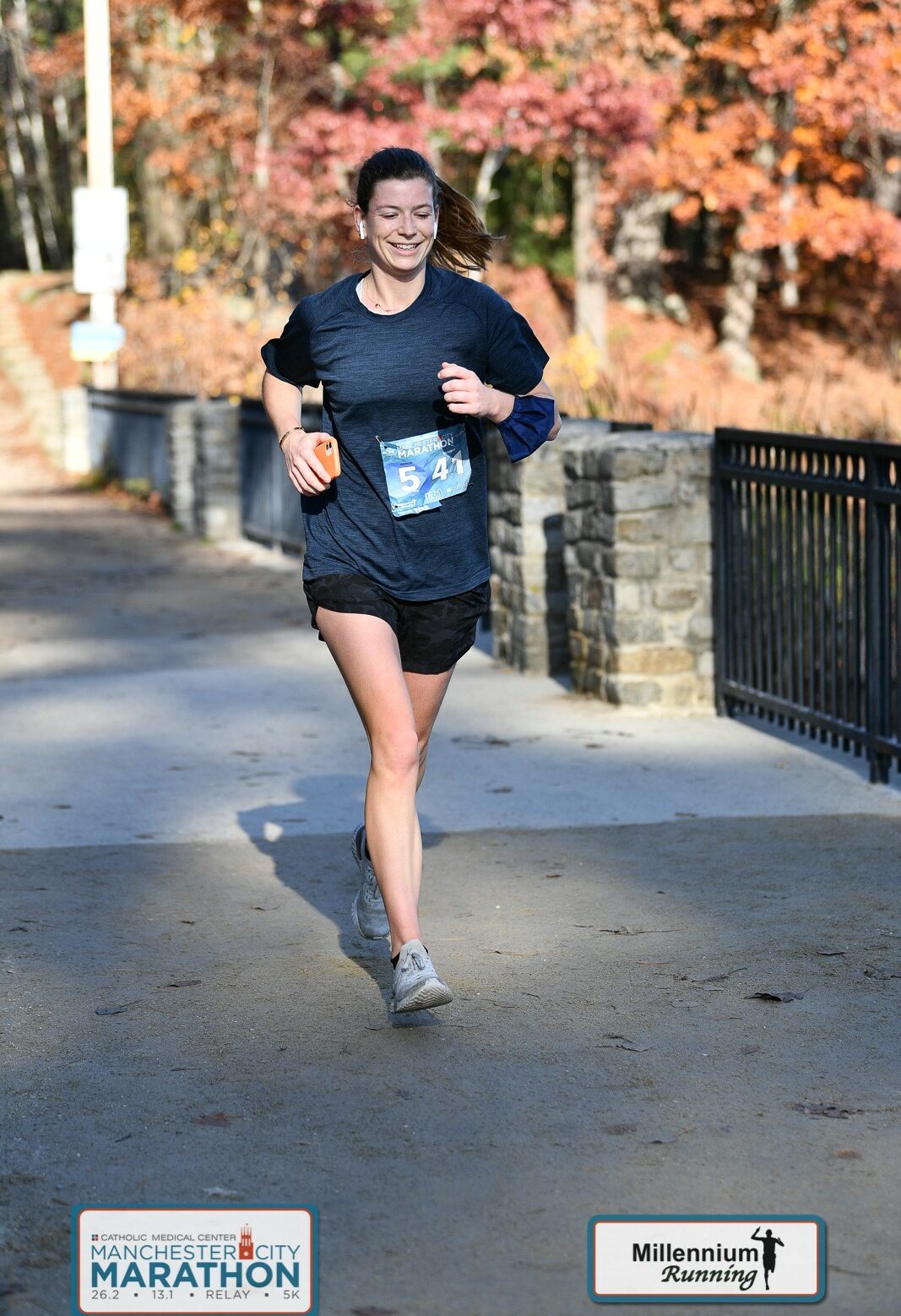 India Dunn, a light-skinned woman, is pictured wearing a dark shirt and running shorts. Trees with colorful leaves are visible in the background.