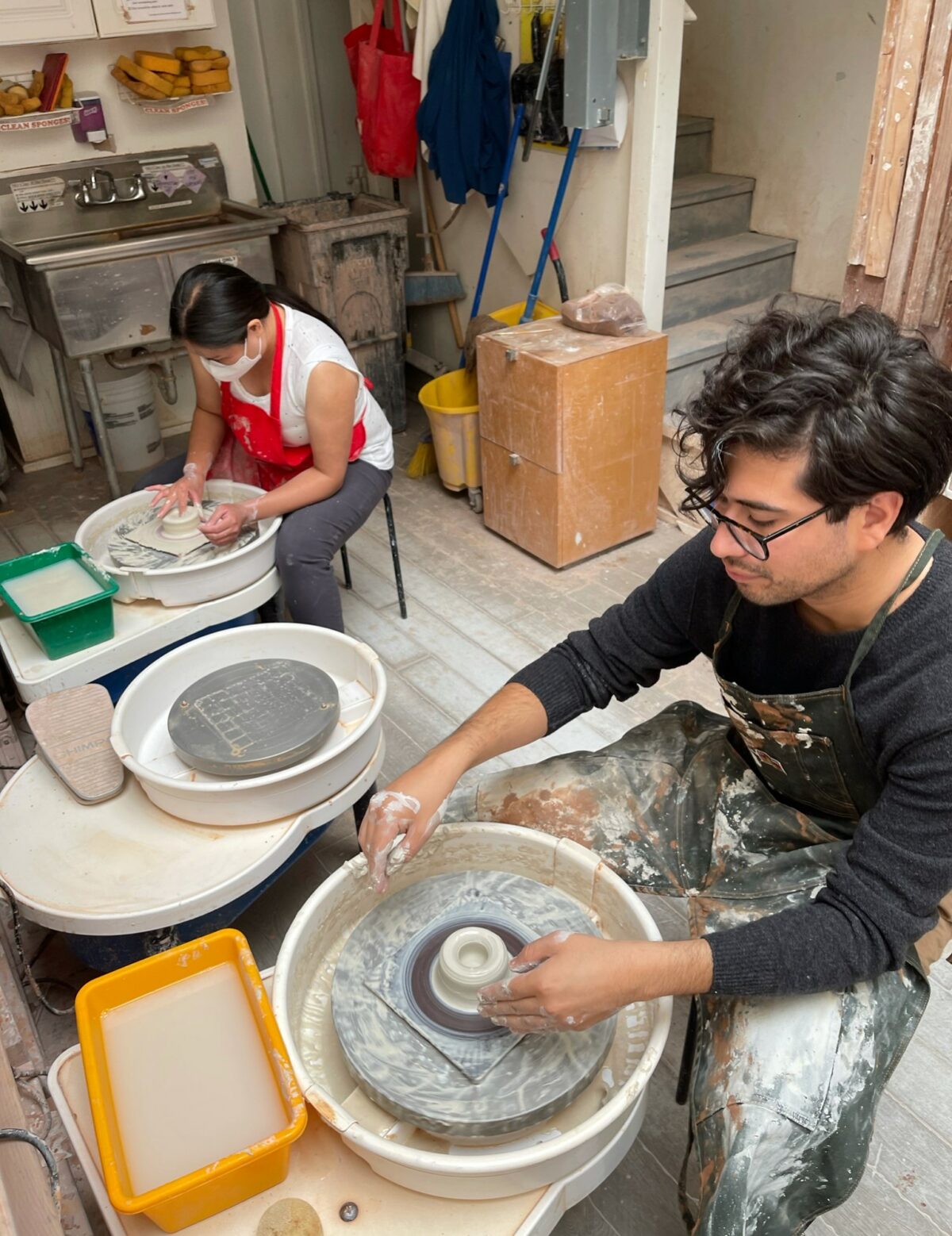 Two people sit over pottery wheels in a studio creating pottery