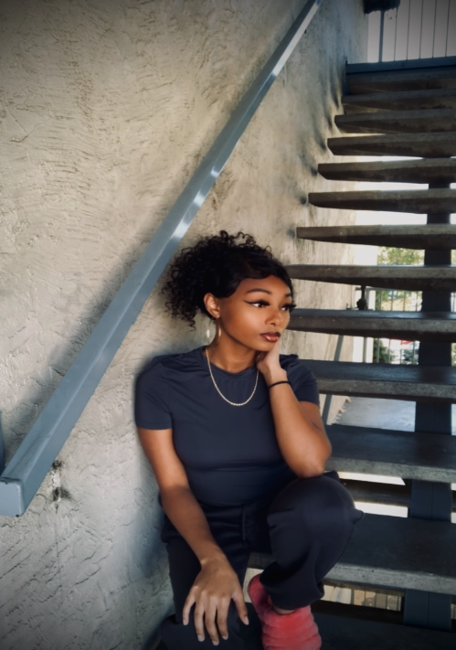 Lia Byrd, a young black woman, is pictured sitting on a staircase. Right hand placed on cheek, left hand is placed on her knee.