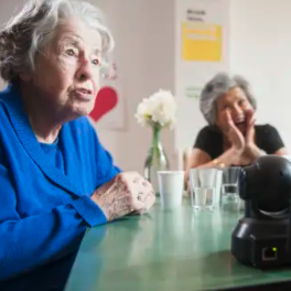 Two elderly, light-skinned women sit at a table that has flowers on it.