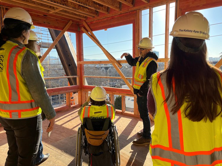 People with and without disabilities wearing construction hard hats and vests visiting a construction site at The Kelsey Ayer Station in San Jose.