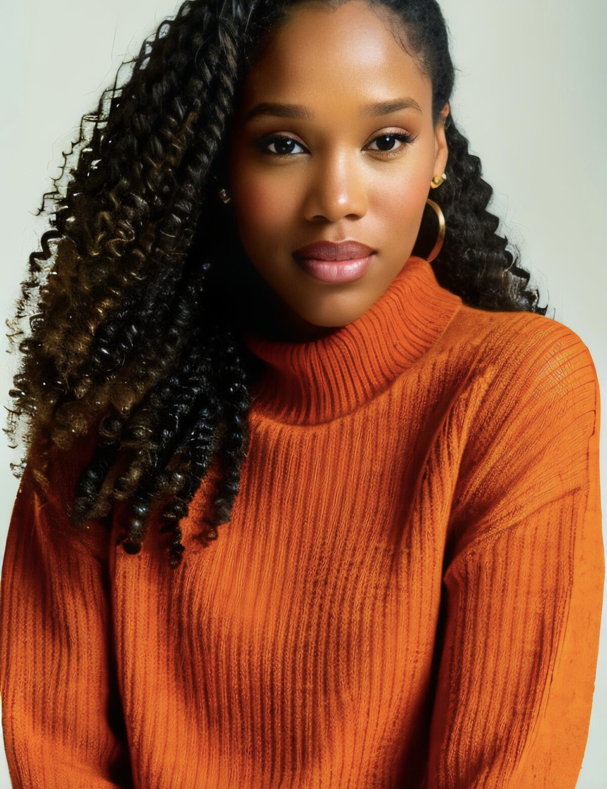 A dark-skinned woman with long, dark, curly hair wearing an orange sweater against a plain background