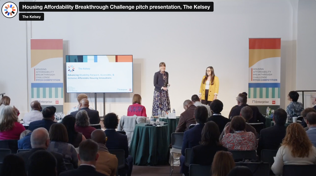 Staff members of The Kelsey, Caroline Bas and Hunter Herrera-McFarland, are pictured on a stage in front of an audience.