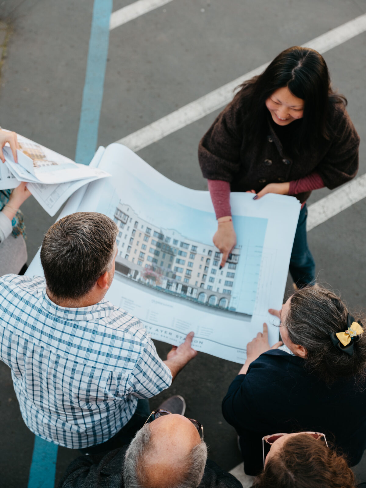 People hold a large piece of paper with the design plans of a building on it.