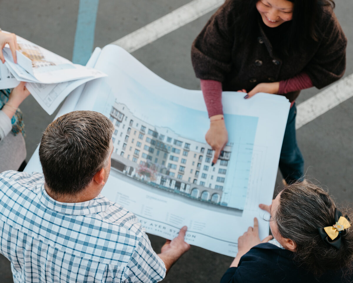 People hold a large piece of paper with the design plans of a building on it.