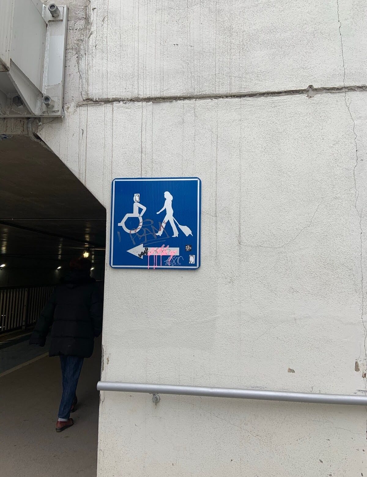 An accessibility sign on a building depicts someone in a wheelchair, and another person carrying luggage.