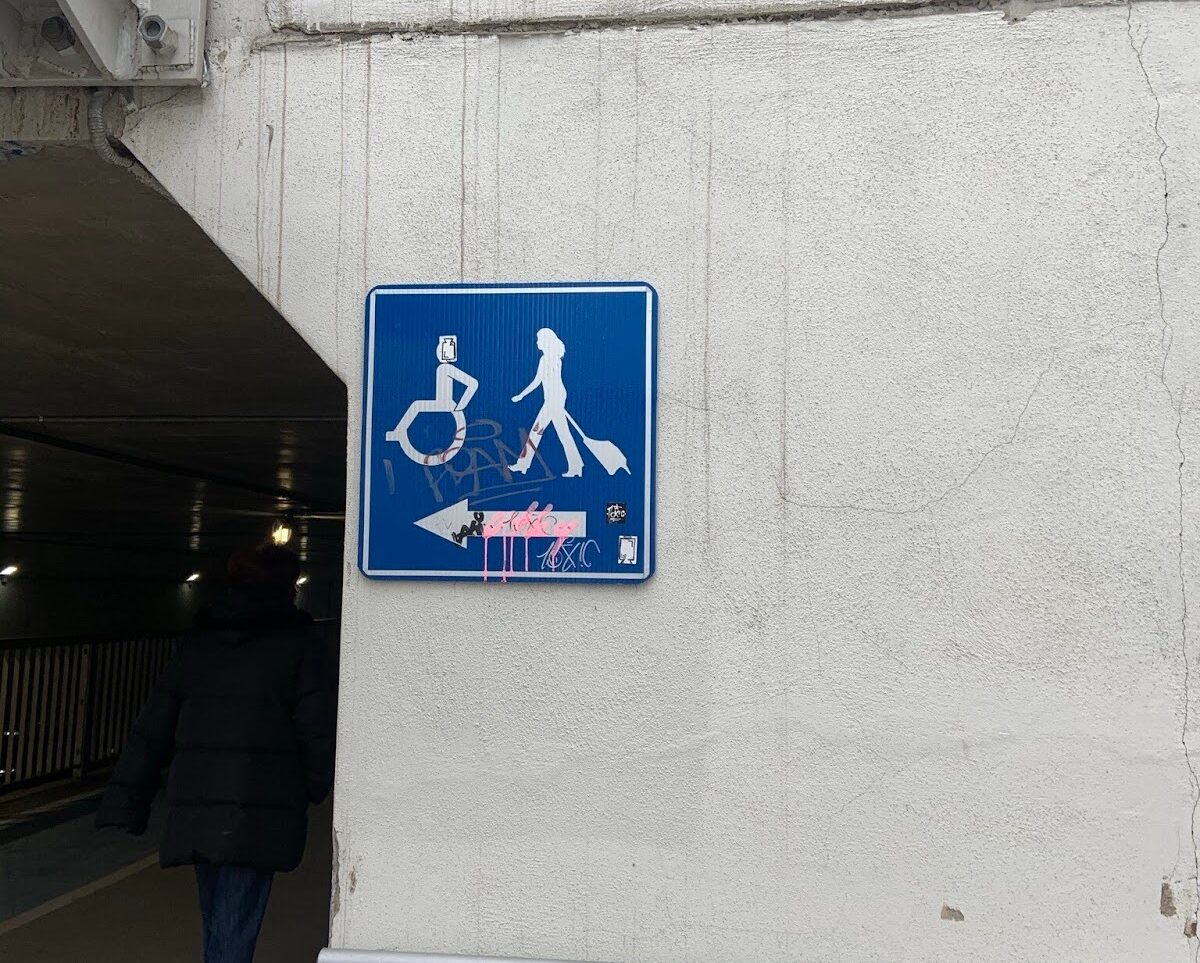 An accessibility sign on a building depicts someone in a wheelchair, and another person carrying luggage.