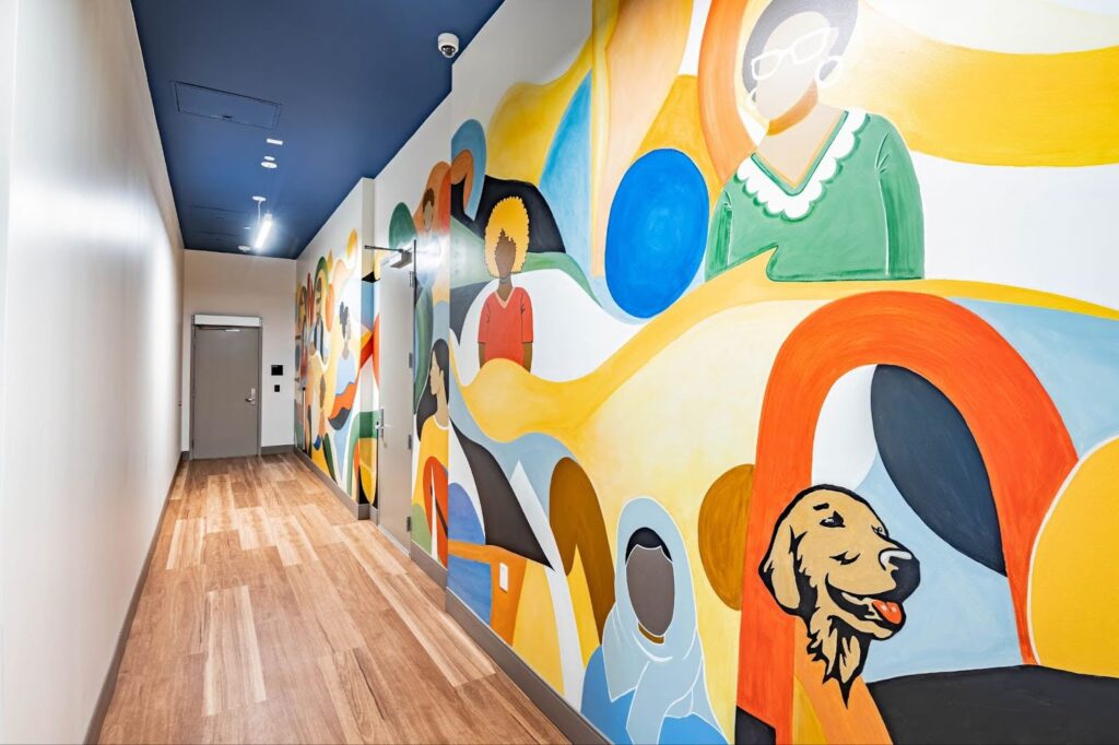 A colorful mural of a diverse group of people and pets in a hallway at The Kelsey Ayer Station. 