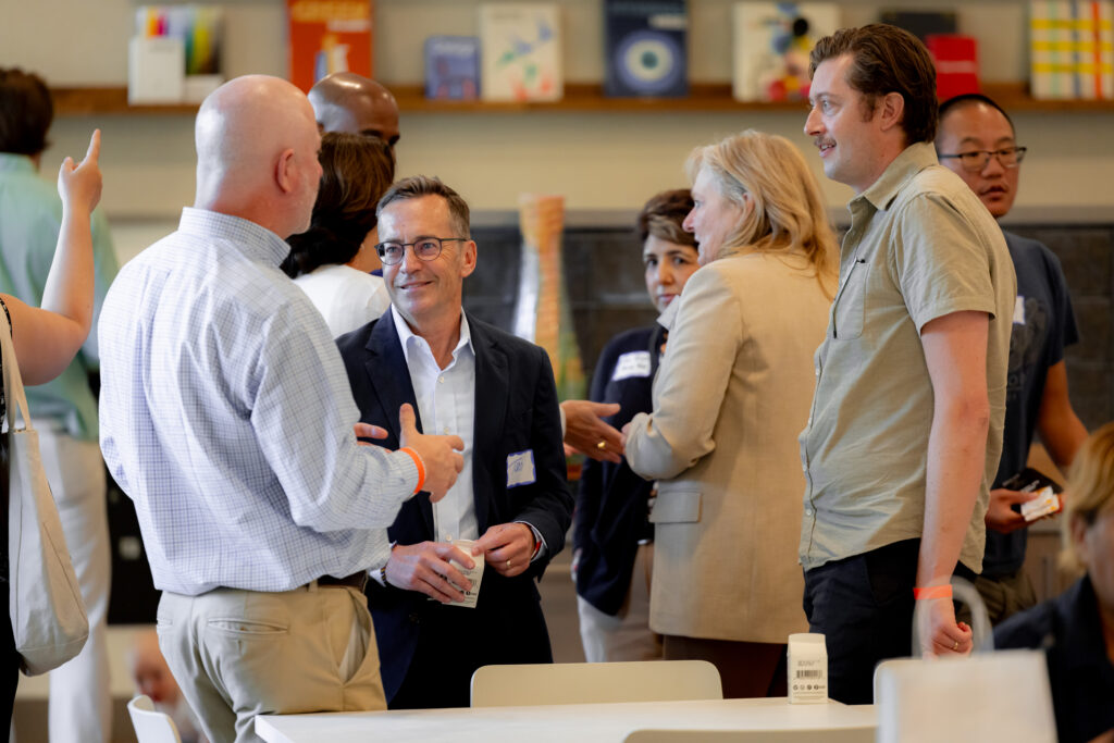 A group of people are pictured mid-conversation. They are gesturing with their hands and some are wearing business clothing, including blazers and button-down shirts.