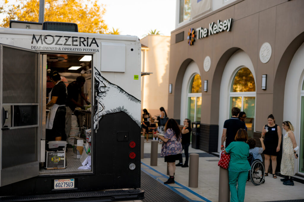 People line up and socialize outside of Mozzeria food truck, a deaf-owned and operated pizzeria. 