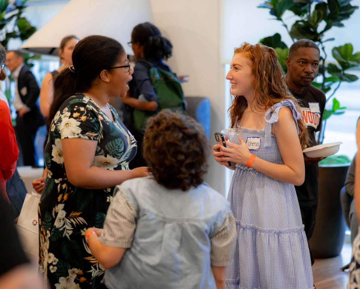 Three people stand and talk happily during a celebration in the lobby of The Kelsey Ayer Station.