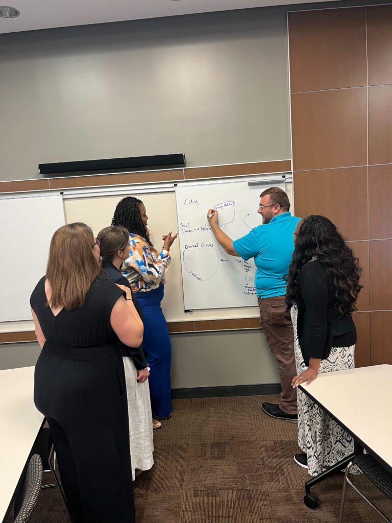 People gather around a large notepad and talk while one person writes on it.