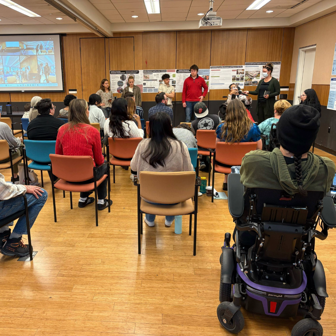 People with and without disabilities present a project to a conference room of people with and without disabilities.