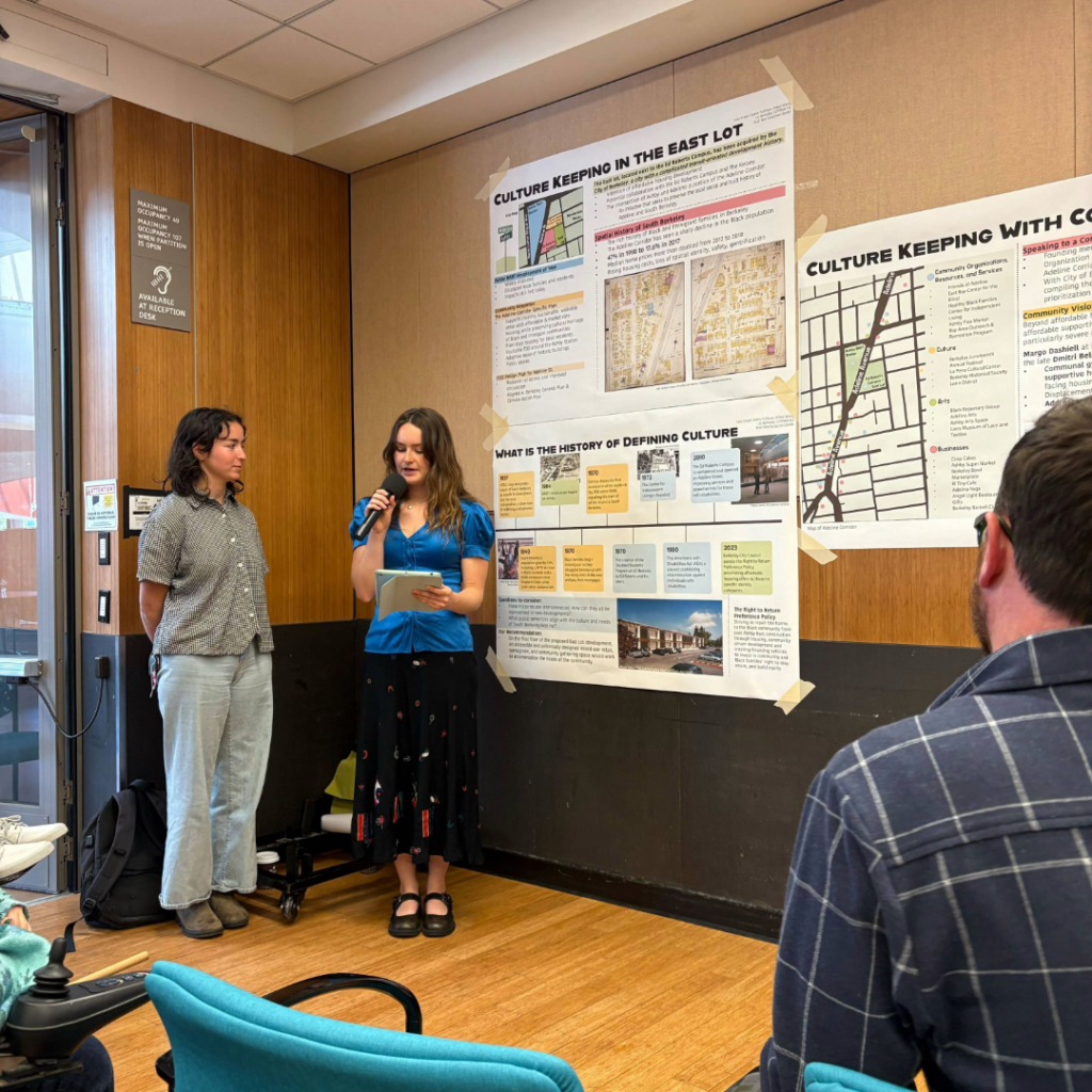Two students present a project. One student holds a microphone.