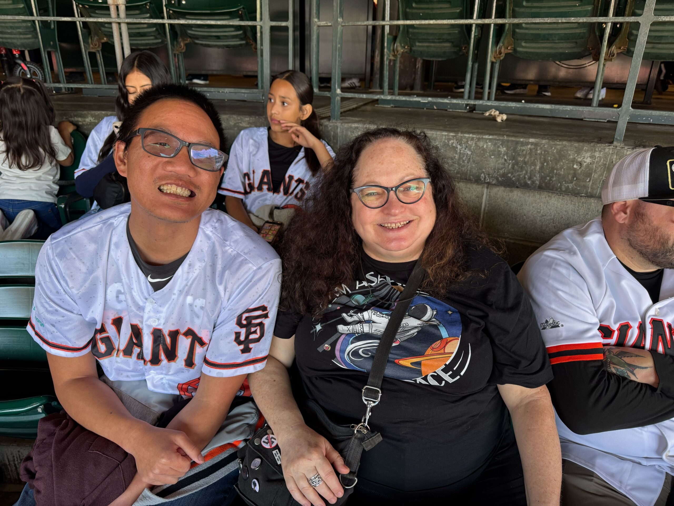 Two residents sit and smile for a picture in the stands at the Giants game. One of them is wearing a baseball jersey.