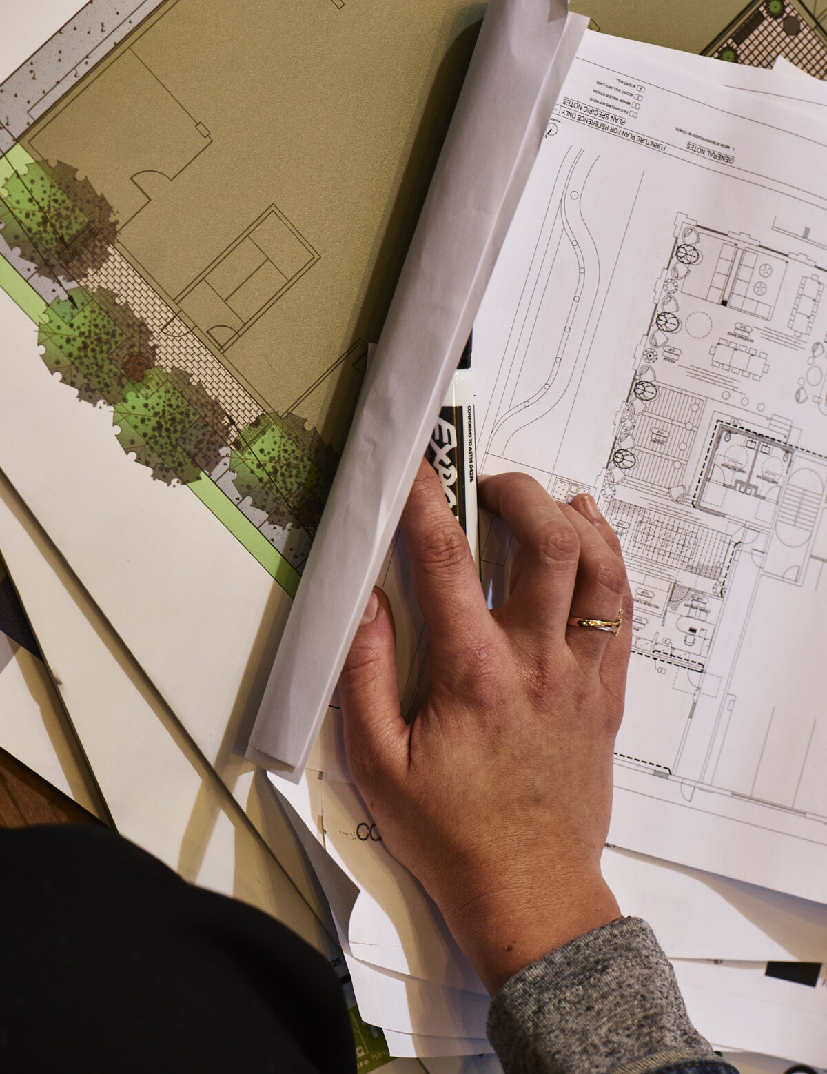A hand holding a dry-erase marker rests on top of several sheets of architectural plans for a multifamily housing development.