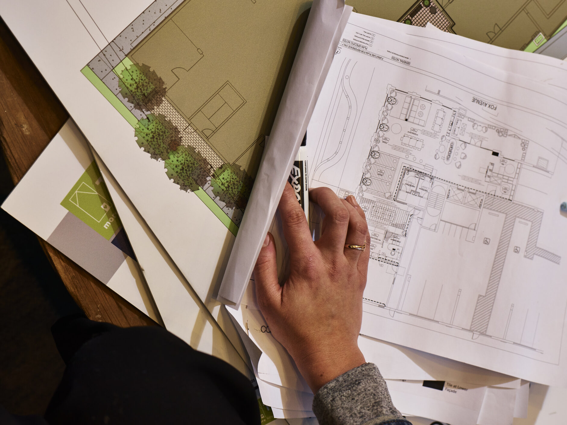 A hand holding a dry-erase marker rests on top of several sheets of architectural plans for a multifamily housing development.