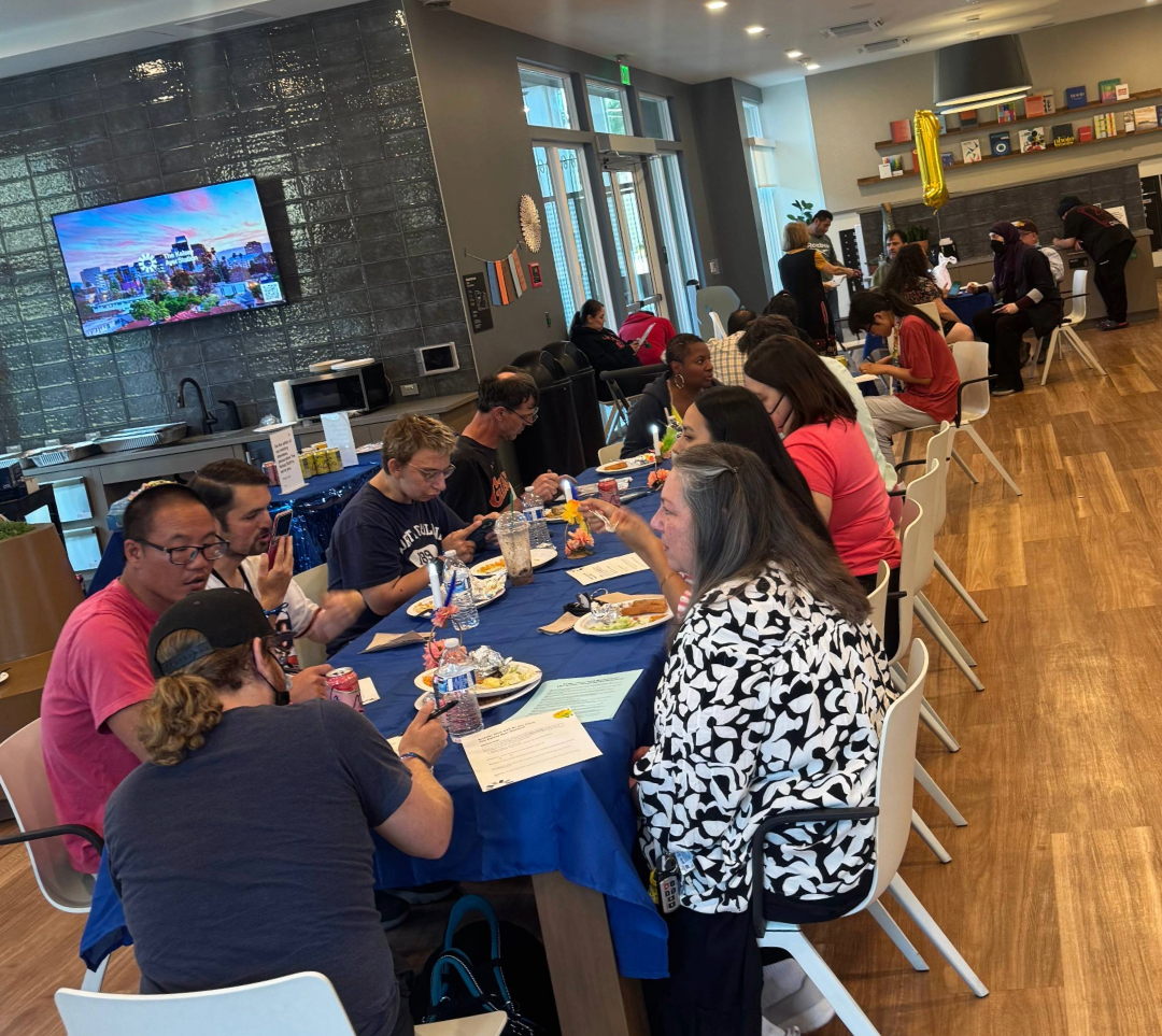 The Kelsey Ayer Station residents eat at a long table in the building lobby for the one-year anniversary of the community opening.