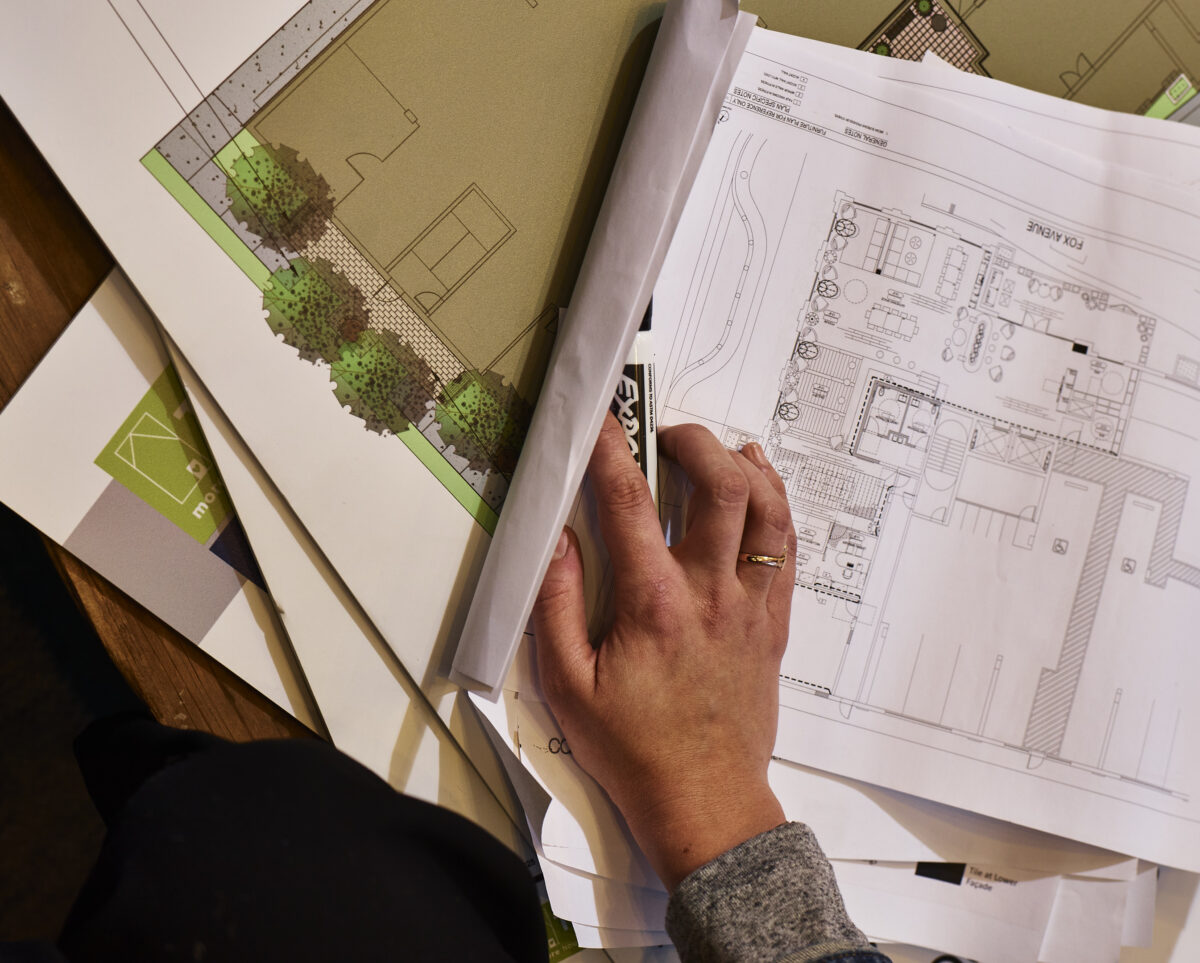 A hand holding a dry-erase marker rests on top of several sheets of architectural plans for a multifamily housing development.
