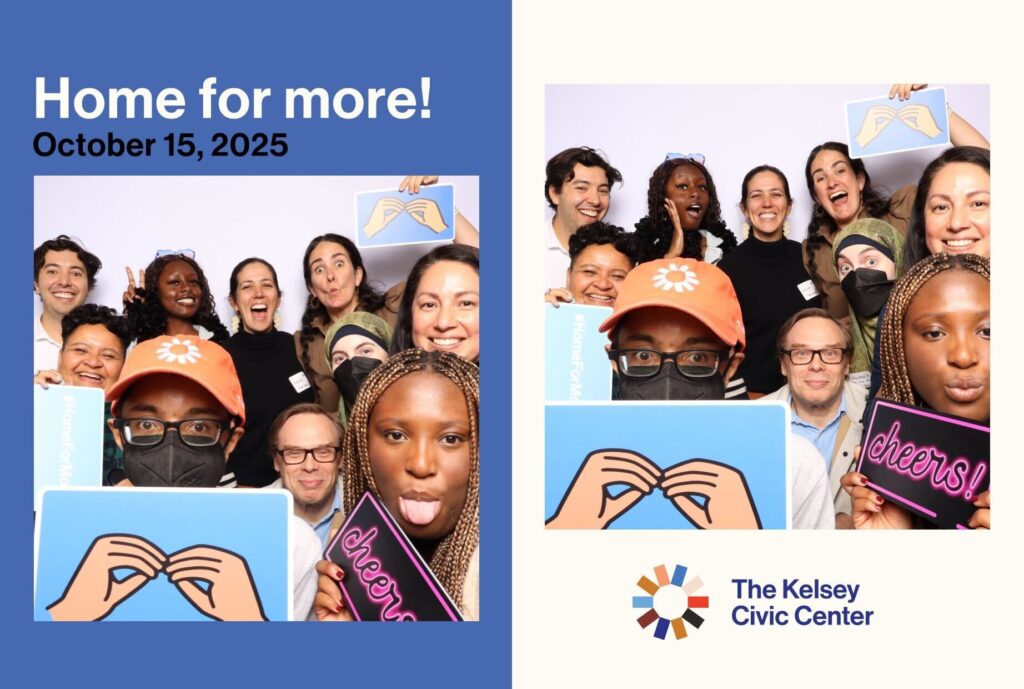 A joyful group photo of The Kelsey team posing together in a photo booth during The Kelsey Civic Center Housewarming event on October 15, 2025. Everyone is smiling and holding playful props, including signs that say “cheers!” and a blue symbol of two hands doing the ASL sign for “more.” The image features The Kelsey Civic Center logo and branding colors in blue, cream, and orange.