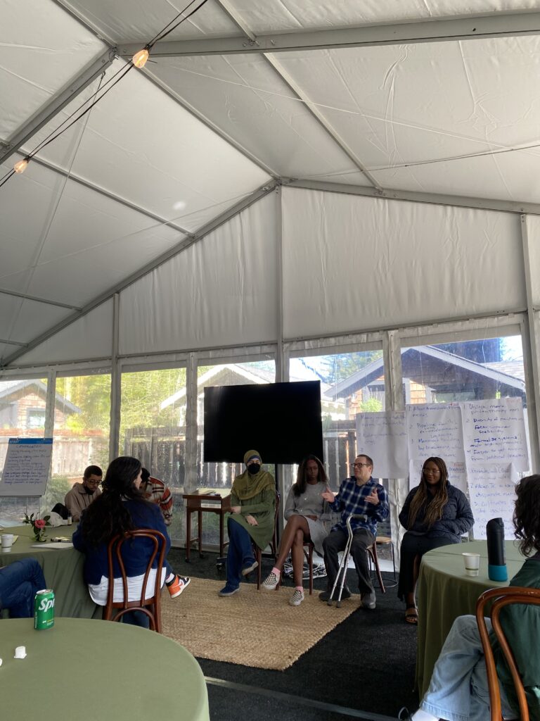 Members of our Resident Service Team with and without disabilities sit in the front of a conference room inside a large tent as they host a question-and-answer session. A TV screen is visible behind them, and other team members sitting around tables are visible in the foreground.