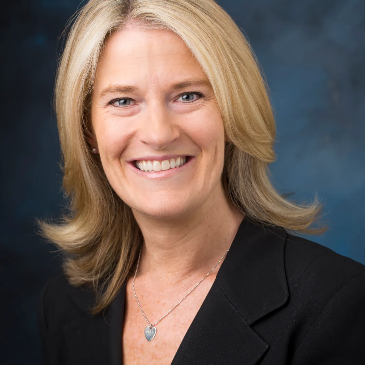 Tara Flynn is a light-skinned woman with light shoulder-length hair. She is pictured wearing a black suit coat and a necklace She is smiling.