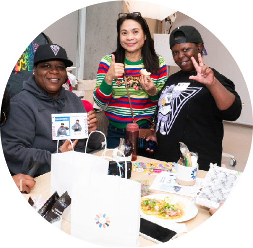 Image of 3 people at standing around a table of food at a gathering.